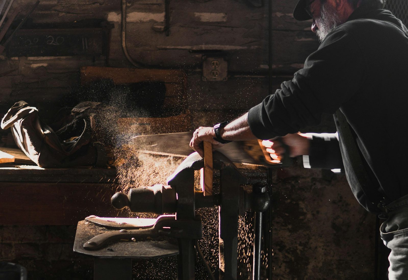 Carpenter cutting a board in a dim workshop with sawdust in the air
