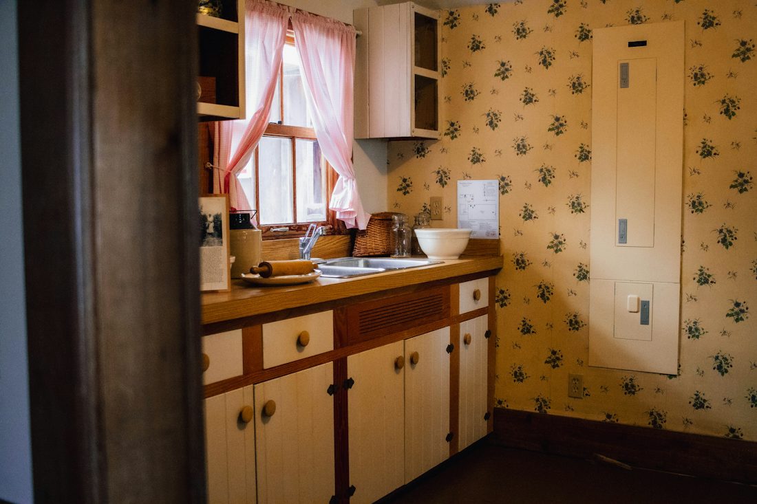 Dated kitchen with floral wallpaper and worn wood cabinets